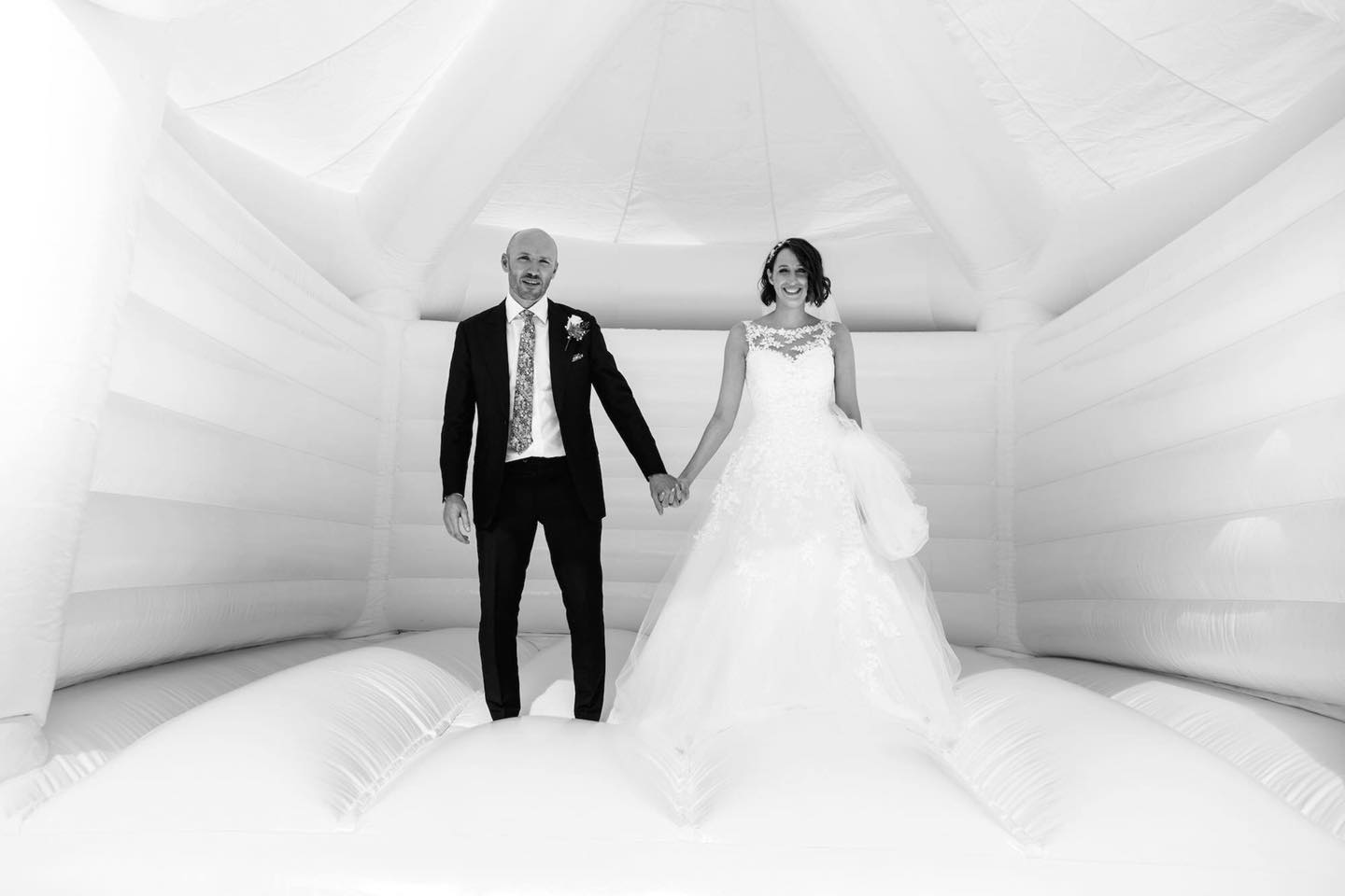 A gorgeous image from a wedding reception of the bride and groom standing hand in hand on a white bouncy castle