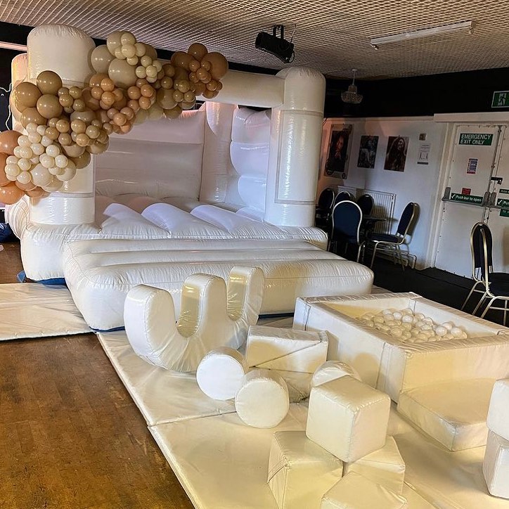 This image shows an indoor white bouncy castle complete with balloon decor and a white soft play set up supplied by SJ's Leisure